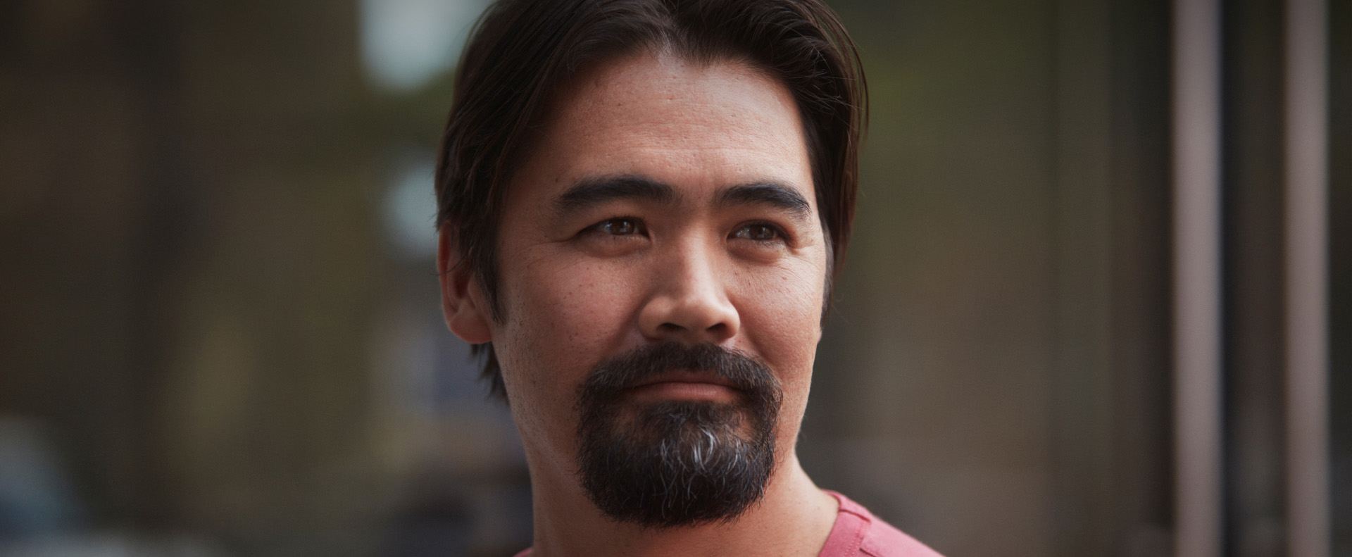 Middle-aged man of asian descent with goatee looking hopeful outdoors