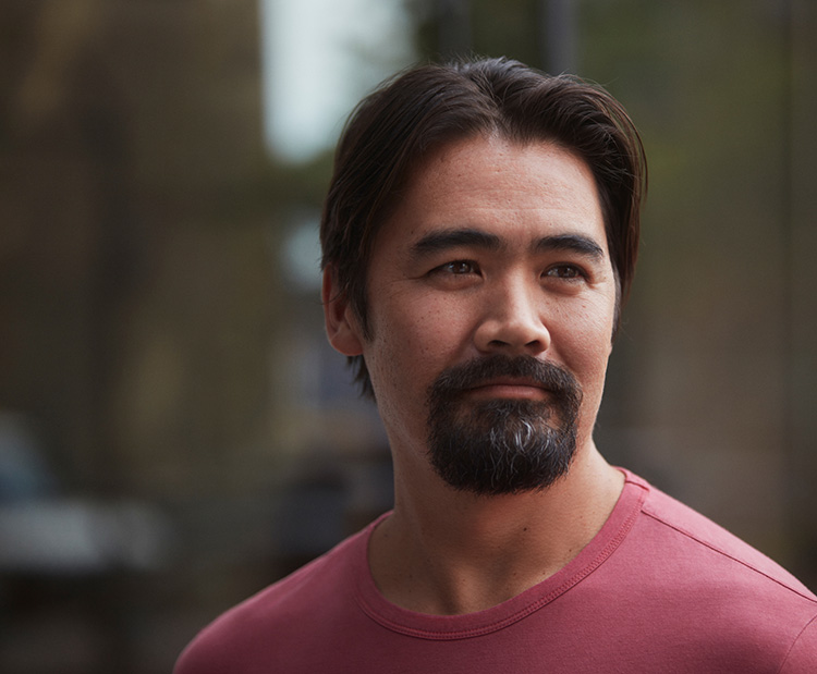 Middle-aged man of asian descent with goatee looking hopeful outdoors