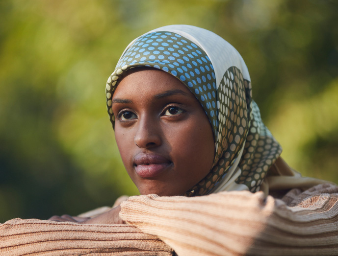 Young woman of color in hijab outdoors looking hopeful with arms folded